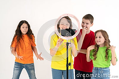 Three teen girls and a boy smiling and shoots a video. Selfies. The phone is mounted on a tripod and the ring lamp shines Stock Photo
