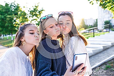 Three teenage schoolgirl girls, summer park, take pictures on smartphone, selfie on phone. Online video call to Internet Stock Photo