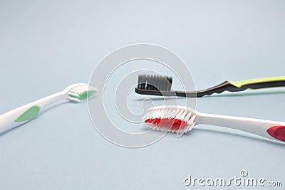 Three tooth brushes on the grey background. Red, black and green toothbrushes. Sanitary hygiene protection, personal care. Stock Photo