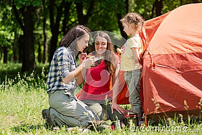 Three tourist females eat near tent outdoors Stock Photo