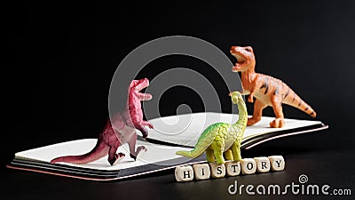 Three toy dinosaurs stand on an open notebook next to the inscription history. The concept of studying history, the Mesozoic era Stock Photo
