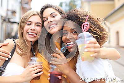 Three trendy cool hipster girls, friends drink cocktail in urban city background Stock Photo