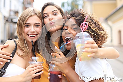 Three trendy cool hipster girls, friends drink cocktail in urban city background. Stock Photo