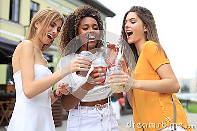 Three trendy cool hipster girls, friends drink cocktail in urban city background Stock Photo