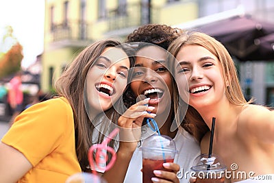 Three trendy cool hipster girls, friends drink cocktail in urban city background. Stock Photo