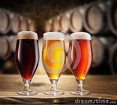 Three type of beer with foam head on wooden table. Blurred brewery cellar at the background Stock Photo