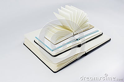 Three unfold notebooks lie on top of each other and fan open small notepad with blank light beige pages. White back Stock Photo