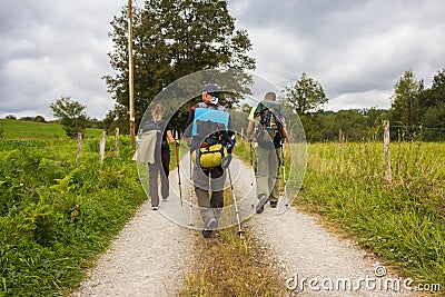 Three unknown pilgrims walking on Camino de Santiago. Group of tourists with backpacks on village road. Active people on the way. Editorial Stock Photo