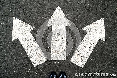 Three white arrows pointing in different directions on gray asphalt floor and black Shoes. Making decisions and making choices. F Stock Photo