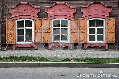 Three windows with the wooden carved architrave in the old wooden house in the old Russian town. Stock Photo