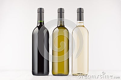 Three wine bottles different colors - transparent, green, black- on white wooden board, mock up. Stock Photo