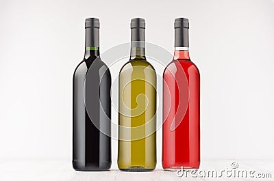 Three wine bottles different colors on white wooden board, mock up. Stock Photo