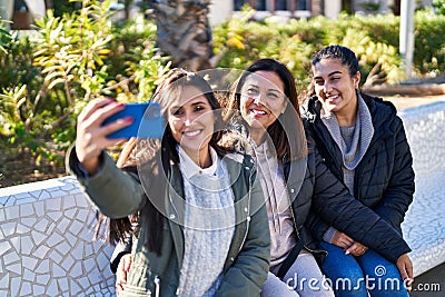 Three woman mother and daughters making selfie by smartphone sitting on bench at park Stock Photo