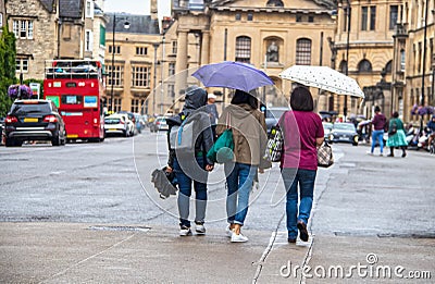 Three women walking away with umbrellas and bags on a rainy day in Oxford England Editorial Stock Photo
