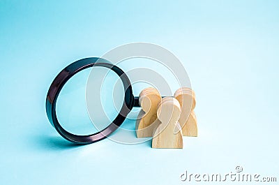 Three wooden human figure stands near a magnifying glass on a blue background. Search for vacancies and work. Human resources, Stock Photo