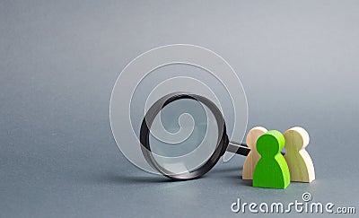 Three wooden human figure stands near a magnifying glass on a gray background. Human resources, management. Stock Photo