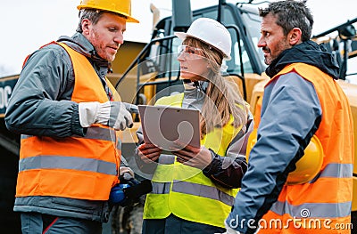 Three workers in a quarry discussing in front of heavy machinery Stock Photo