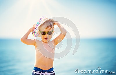 Little boy smiling at the beach in hat with sunglasses Stock Photo