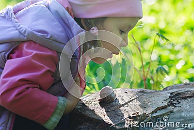 Three years old preschooler girl blowing on crawling edible snail Stock Photo