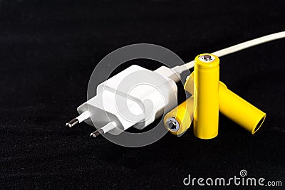 Three yellow batteries and battery charger plug close-up on a dark black blurred background. Electrics. Battery power. Accumulato Stock Photo