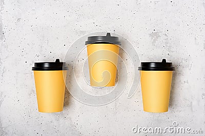 Three yellow paper cups, light gray concrete background. Minimalism concept. Place for text. Flatlay. Coffee to go Stock Photo