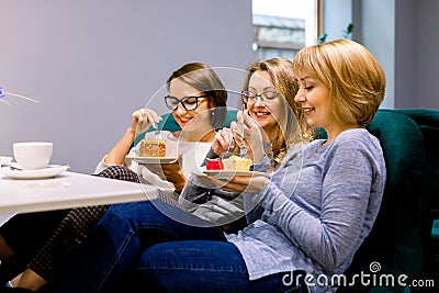 Three young beautiful Women sitting on the sofa in cafe indoors and Having lunch In Cafe. Women eating cakes and having Stock Photo