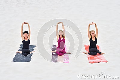Three young beautiful women sitting in yoga pose Gomukhasana Stock Photo
