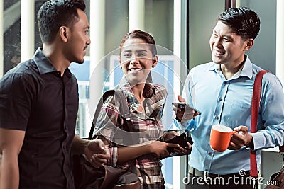 Three young and cheerful employees at their workplace talking in the morning Stock Photo