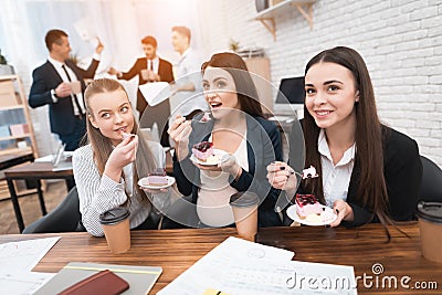 Three young girls eating sweet cake at lunchtime in office. Lunch break. Stock Photo