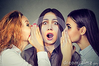 Three young women telling whispering a secret gossip each other in the ear Stock Photo