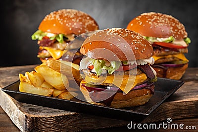Three yummy grilled burger with double meat cutlet and fries on a wooden table, side view. Stock Photo
