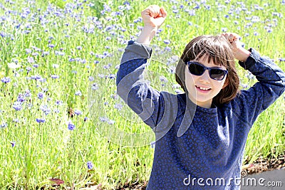 Thrilled young girl with blue sunglasses over spring cornflower field Stock Photo