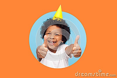 Thumbs up to birthday party! Excited amazing joyful boy with funny cone on head showing like Stock Photo
