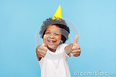 Thumbs up to birthday party! Excited amazing joyful little boy with funny cone on head showing like gesture Stock Photo
