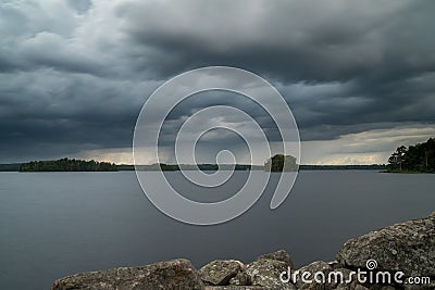 Thunderstorm with beautiful rainfall and dark clouds over a lake in sweden and rocks in the forground Stock Photo