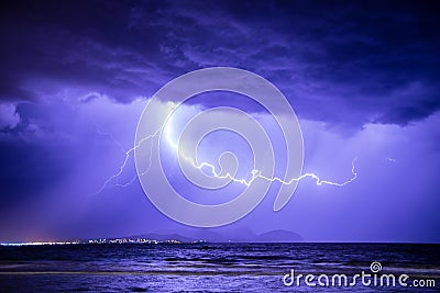 Thunderstorm with lightning at dramatic sky over sea on coast with mountains in the background Stock Photo