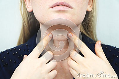 Thyroid gland. Closeup portrait of cute sick young blonde woman in white top having sore throat, holding hand on her neck Stock Photo