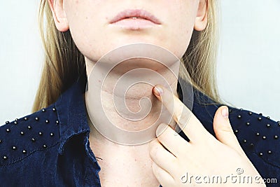 Thyroid gland. Closeup portrait of cute sick young blonde woman in white top having sore throat, holding hand on her neck Stock Photo