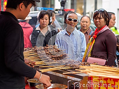 TIANJIN, CHINA - 6 OCT 2019 - Chinese customers wait for their order of Xinjiang style grilled lamb skewers at a food stall Editorial Stock Photo