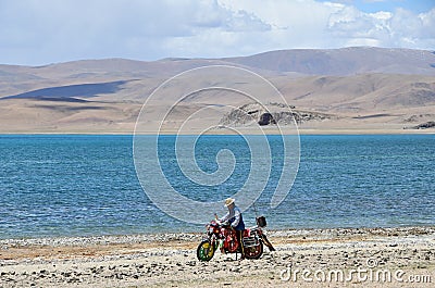 Tibet, China, June, 06, 2018. Shepherd on motorbike on the shore of lake Gomang in the summer Editorial Stock Photo