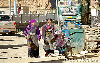 Two senior women in colorful traditional clothes walk down the unpaved street. Editorial Stock Photo