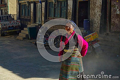 CLOSE UP: Local Asian woman crosses the dusty street in a rural town in Tibet Editorial Stock Photo