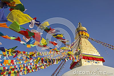 A Tibetan Buddhist Stupa Bodhnath with eyes and multicolored prayer flags against a clean blue sky at daytime Stock Photo