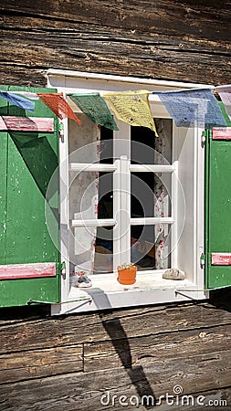 Tibetan prayer flags on green shutters and white window on typical and traditional austrian alpine wooden house - Salzkammergut Stock Photo