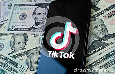 TikTok app logo on the smartphone screen and US dollar bills next to it. Conceptual photo Editorial Stock Photo