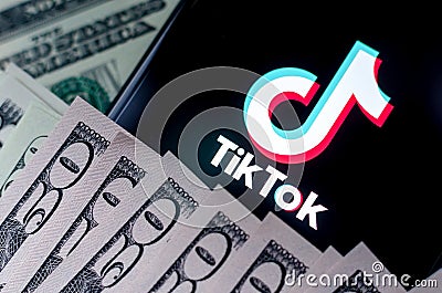 TikTok app logo on the smartphone screen and US dollar bills next to it. Conceptual photo Editorial Stock Photo