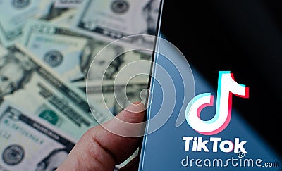 TikTok app logo on the smartphone screen and US dollar bills next to it. Editorial Stock Photo