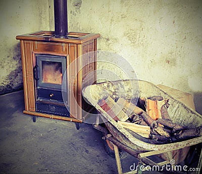 Tiled stove and wheelbarrow full of firewood with vintage effect Stock Photo