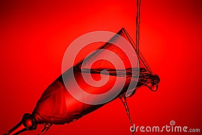 Tilted full champagne glass close-up with frozen water jets and splashes in bright red backlight. Stop motion photography Stock Photo