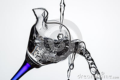 Tilted full cocktail glass on blue leg with frozen water jets and splashes in white backlight close-up. Stop motion photography Stock Photo